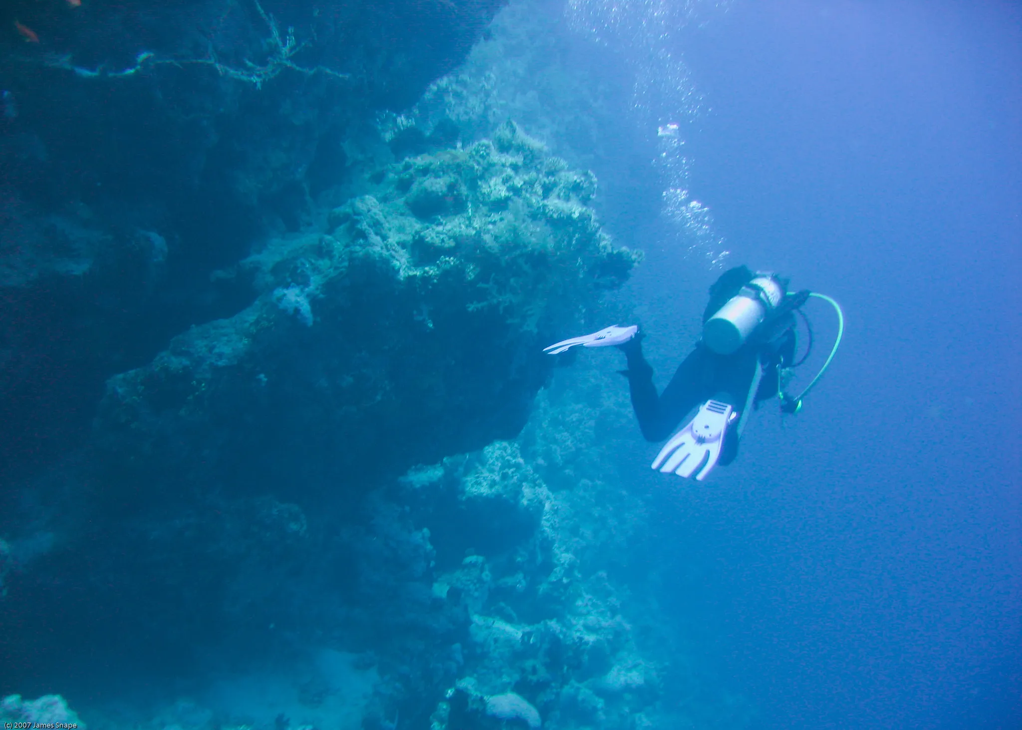 Photo of a scuba diver swimming away from the camera at 30m depth. Blue hues throughout the photo due to light filtering at depth.